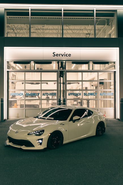 Elegant white sports car parked in front of a service center at night, illuminated by soft lighting.