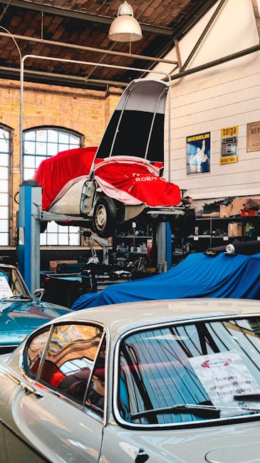 A vintage car workshop featuring classic cars on lifts, covered and maintained indoors.